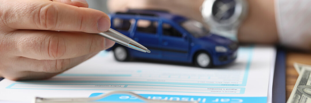 Male hands hold ballpoint pen over car insurance blank and toy car. Car insurance concept.