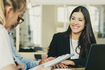 Couple of customers meeting with agent and reading insurance agreement. Young woman in formal jacket smiling and looking at clients. Business meeting concept