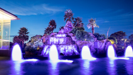 Colourful water fountain at night dark blue skies green palms 