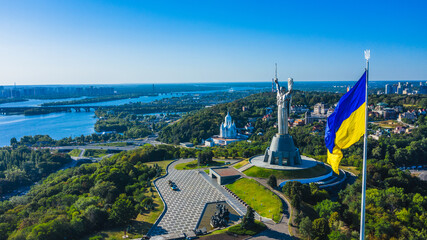 Obraz na płótnie Canvas Aerial view to the Beautiful landscape city Kiev with a Dnepr river. Top view to the Motherland statue in the Kiev. The well-known landmarks in Kyiv. Closeup National flag og Ukraine.