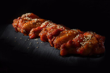 chicken wings in a sweet sauce sprinkled with sesame seeds on a black background, pepper lies on top