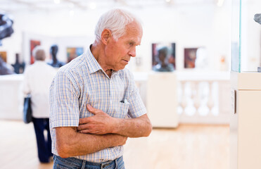 mature European man examines paintings in an exhibition in hall of an art museum