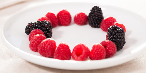 raspberries and blackberries laid out on a white plate in circle