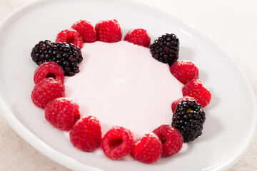 fresh raspberries and blackberries laid out on a white plate in circle with yogurt