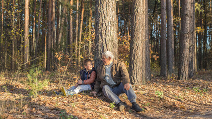 Naklejka na ściany i meble Happy child with Grandfather playing at the forest. Grandpa retiree. Retirement parent. Portrait of pensive senior man and his grandson. Senior man having fun with his grandchild outdoor.