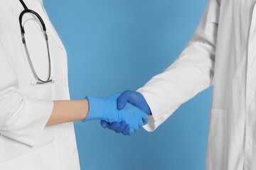 Doctors shaking hands on light blue background, closeup