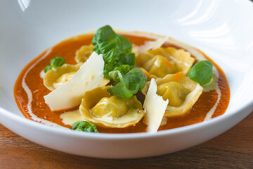 Homemade tortelli with tomato sauce , basil , parmesan shaving and sauce.