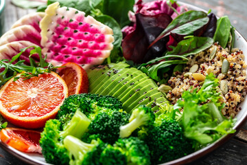Healthy vegetarian buddha bowl salad with vegetables, avocado, blood orange, broccoli, watermelon radish, spinach, quinoa, pumpkin seeds. Food recipe background. Close up