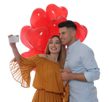Lovely couple with heart shaped balloons taking selfie on white background. Valentine's day celebration