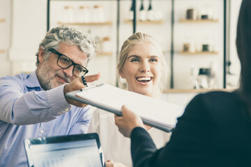 Insurance agent meeting with young and mature customers at co-working, giving agreement for signing. Businesswoman using laptop with graphs on display. Business meeting concept