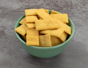 Cheese and garlic snack crackers in a green bowl on a gray mottled background side view.
