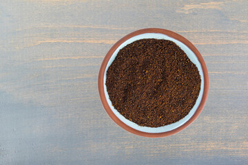 Top view of a small terracotta spice bowl filled with chili powder on a blue painted wood background.