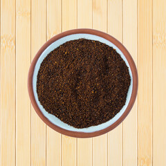 Top view of a small terracotta spice bowl filled with chili powder on a wood background.