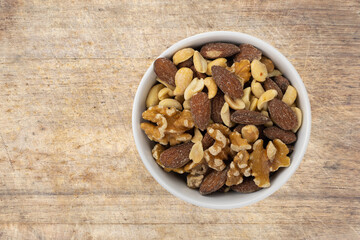 Top view of assorted nuts in a white bowl atop an old wood cutting board.