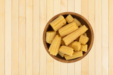 Top view of a wood bowl filled with canned organic baby corn offset on a wood placemat.