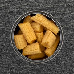 Top view of an open can filled with organic baby corn on a gray slate background.