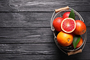 Whole and cut red oranges on black wooden table, top view. Space for text