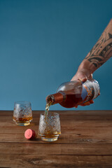 Pouring German rye whiskey in two glasses on wooden table with blue background