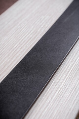 A black leather belt lies on a white tree diagonally close-up