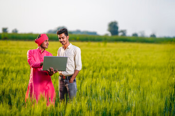Young Indian agronomist or banker showing some information to farmer in laptop at wheat field