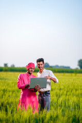 Naklejka na ściany i meble Young Indian agronomist or banker showing some information to farmer in laptop at wheat field