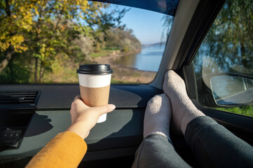 Female hand holding a cup of coffee in a car, nature