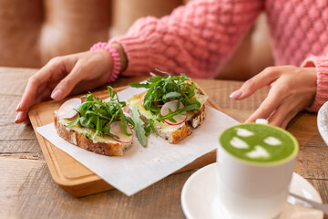 Woman in a restaurant in a cozy warm sweater wholesome breakfast with toast with arugula and salmon