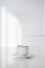 A white cup and saucer stands on a table against a light background