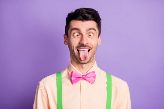 Photo of childish fooling young man dressed yellow shirt showing tongue out looking nose isolated purple color background