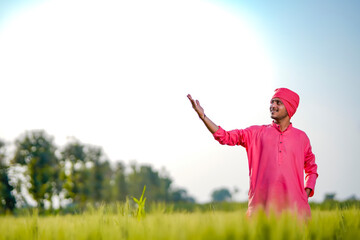 Young indian farmer standing his wheat field and giving happy expression