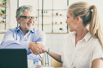 Obraz premium Businessman meeting and shaking hands with insurance agent at co-working, sitting at open laptop, smiling, discussing agreement. Medium shot,. Handshake or cooperation concept