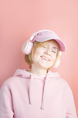 Caucasian girl in a pink sweatshirt and with pink headphones on a background similar in tone. Concept for music, podcasts, audiobooks. World Music Day, World Rock-n-roll Day..