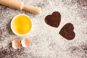 Sprinkled flour with two hearts painted on a wooden background, with a rolling pin and eggs. Baking recipes. Valentine's day concept. Declaration of love