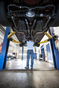 Mechanic in a repair shop works on the underside of a car up on a lift