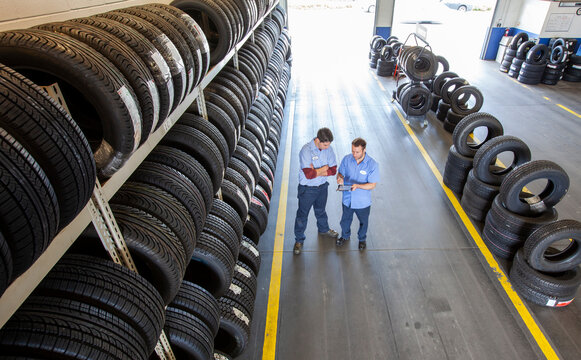 Two mechanics working the tire area of an auto repair shop, using a digital tablet