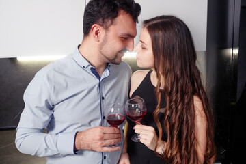 Close up couple of lovers holding glasses with red wine, touching foreheads, enjoying romantic date, standing in kitchen, celebrating relocation or anniversary or valentines day