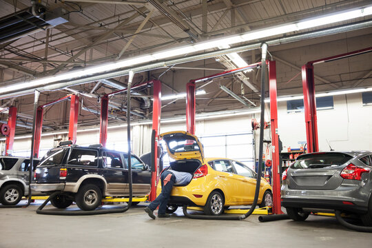 Torso of an mechanic leaning into the trunk of a car, working in an auto repair shop - Powered by Adobe