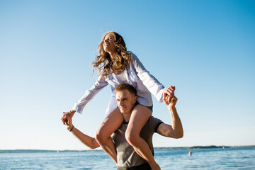 a girl sits on the shoulders of her beloved guy for a walk near the sea, a loving couple spends...