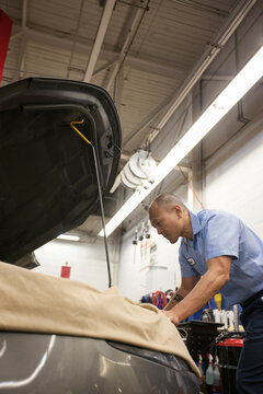 Pacific Islander mechanic works on the engine compartment in an auto repair shop