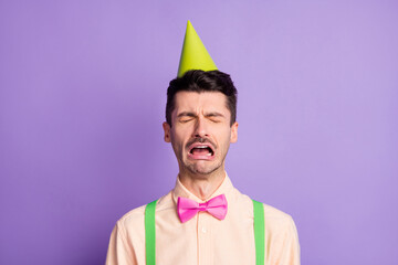 Photo of upset offended young guy wear yellow shirt birthday cap crying nobody came isolated violet...