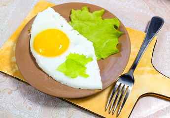 Fried eggs on a plate on the table with a green lettuce leaf.