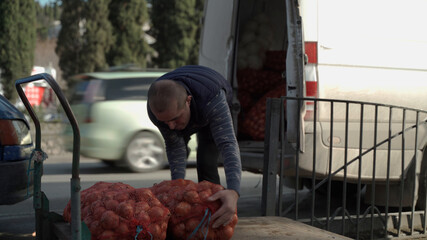 Portrait of a Caucasian nationality male loader worker loading large bags of bow on a cart