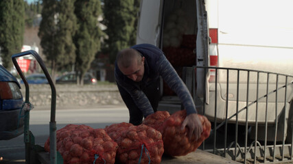 Portrait of a Caucasian nationality male loader worker loading large bags of bow on a cart