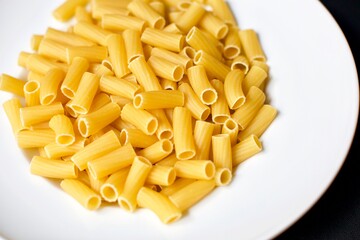 Uncooked rigatoni pasta in the white porcelain plate. Blurry background.