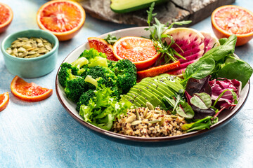 Quinoa bowl salad with vegetables, avocado, blood orange, broccoli, watermelon radish, spinach, pumpkin seeds. Food recipe background. Close up