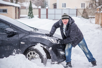 Winter, people and car problem concept. Man try on pushing the car, stuck in the snow. Mutual aid. Winter problem. transportation, winter and vehicle concept - closeup of man pushing car stuck in snow