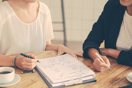 Young female colleagues meeting and discussing business plan, writing strategy scheme on paper, making draft. Cropped shot. Planning concept