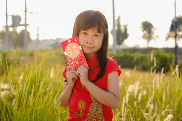 Little girl wearing red traditional Chinese cheongsam with holding red envelope in the backyard is happy, sentence is Chinese always wish people Happy Chinese New Year..