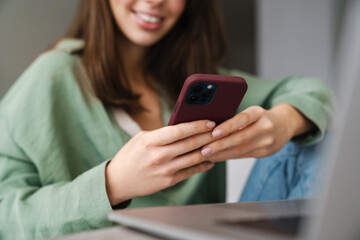 Cheerful beautiful woman using mobile phone while working with laptop