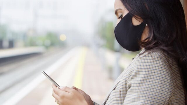 Focus pulls from foreground to background as businessman and businesswoman wearing face masks on train station platform looking at mobile phones - shot in slow motion